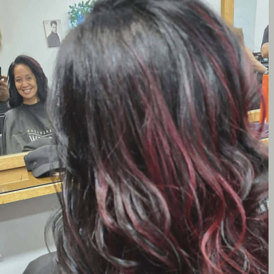 Mèches cerise sur cheveux bruns, cliente souriante au miroir